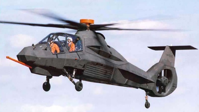 An RAH-66 Comanche prototype flying against a light blue sky with clouds