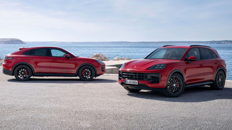 Front three-quarters shot of a red Cayenne GTS parked in front of a side view of a red Cayenne GTS Coupe parked in front of a body of water