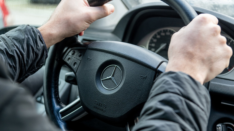 A close up of a Mercedes-Benz steering wheel with a driver's hands.
