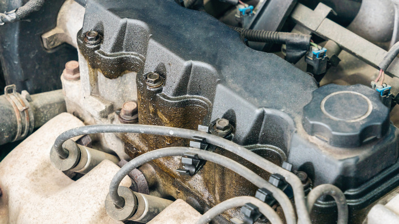 Old four-cylinder car engine with visible oil stains on the valve cover.