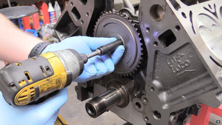 A man with blue nitrile gloves and a yellow cordless screwdriver puts a timing gear on a GM 5.3-liter or 4.8-liter Vortec V8