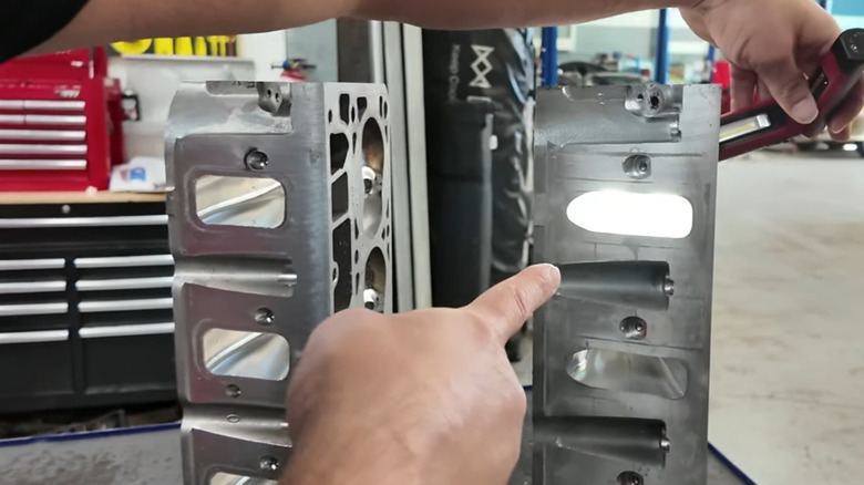 A head with rectangular ports and a head with cathedral ports sitting on a bench with a technician's hands and flashlight pointing at the differences