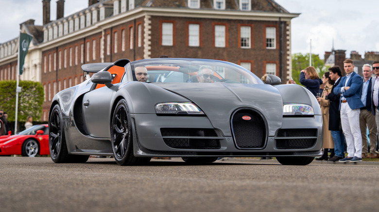 A gray Bugatti Veyron Super Sport being driven through a crowd during a car show.
