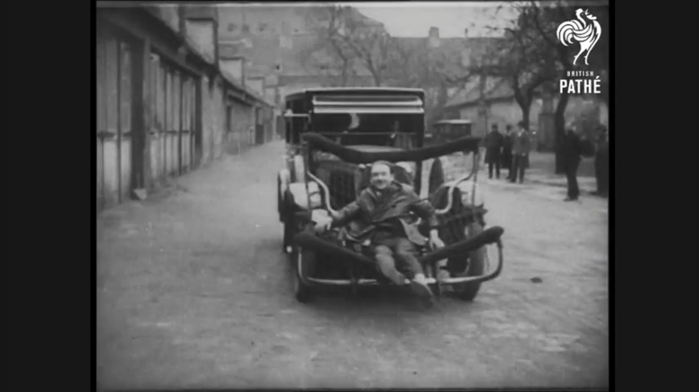 A man smiles, sitting within the basket of a pedestrian catcher device affixed to the front of an automobile in 1927.