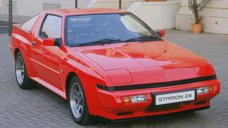 A red Mitsubishi Starion parked in front of a building.