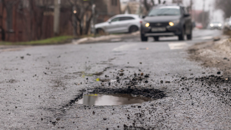 A pothole in the road with a vehicle driving toward it