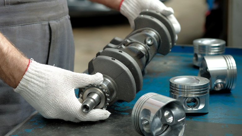 A crankshaft held by a technician next to pistons on a table