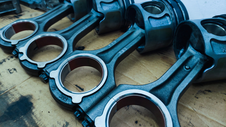 Four connecting rods with pistons attached on display.