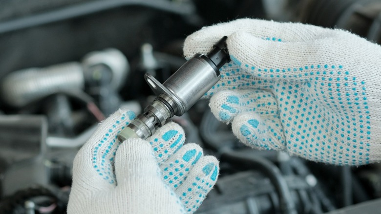 A mechanic's hands holding a new valve for a Toyota VVT system