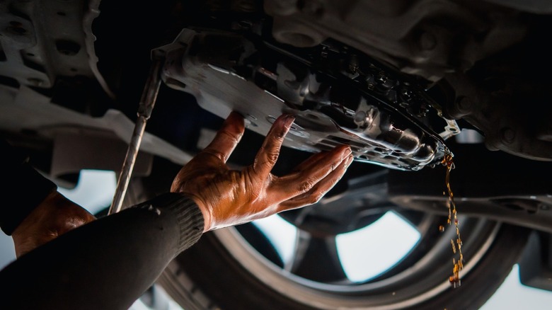A mechanic's gloved hand dropping a transmission pan to change the fluid