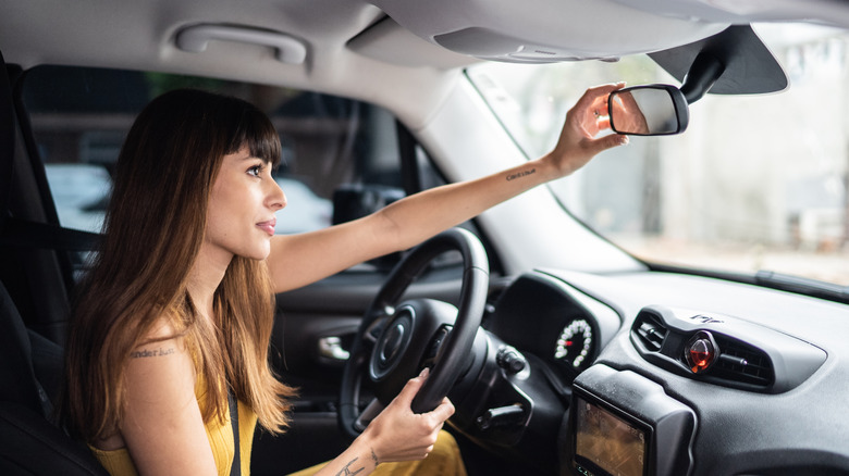 A woman adjusts the rearview mirror in a car.