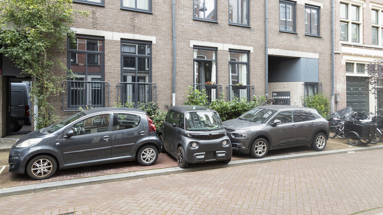 A tiny car parked perpendicularly between two parallel parked cars on a Dutch street