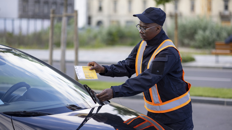 A parking enforcement officer placing a ticket under the windshield wiper of an illegally parked car