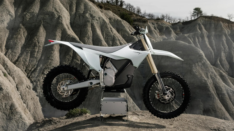 A white Stark Varg EX parked on a stand with rough rocky terrain in the background