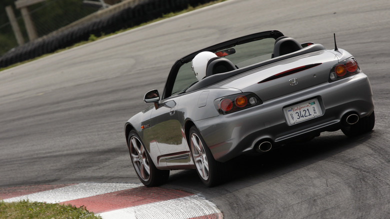 A rear 3/4 view of a silver 2009 Honda S2000 on a racetrack.