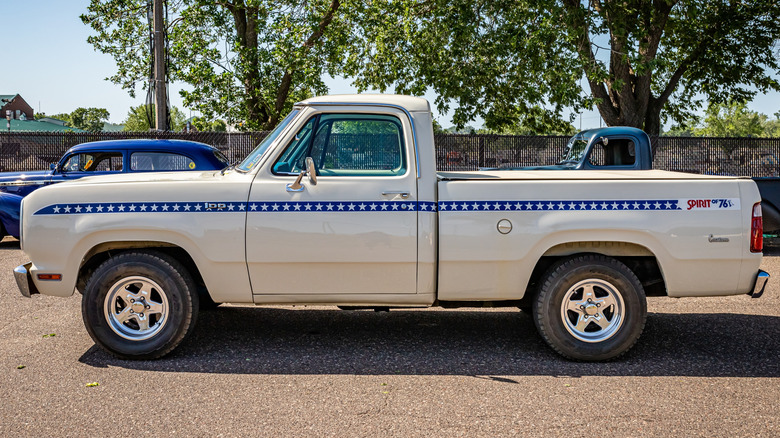 A white customized 1975 Dodge D100 pickup at a collector's car show.
