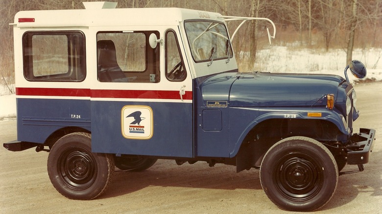 A DJ5 postal Jeep on a road in front of trees and snow