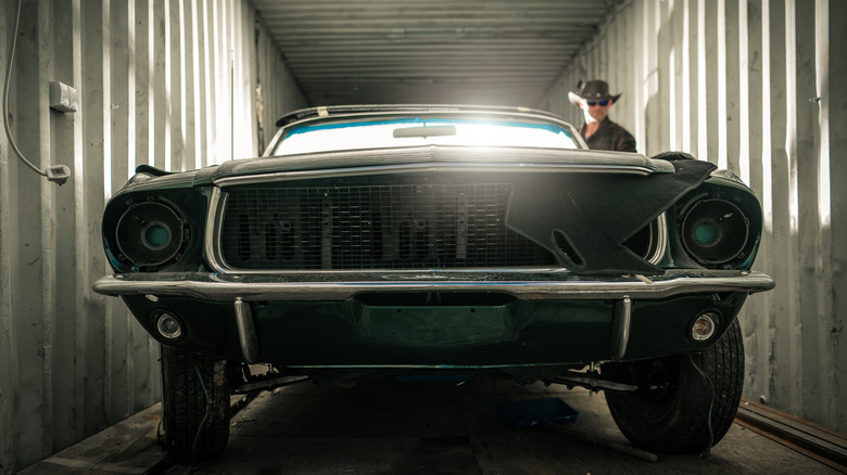 An old, damaged Ford Mustang parked inside a shipping container, shown from the front.