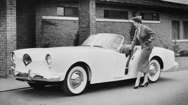 A woman sliding open a Kaiser Darrin drivers door in black and white