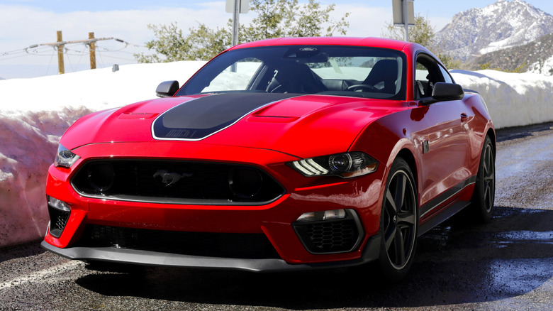 An S550-generation red Ford Mustang Mach 1 parked on a mountain road surrounded by snow.