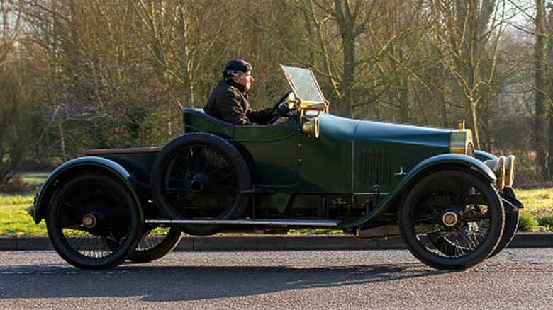 An elderly gentleman driving a Ford Model T on a quiet British road