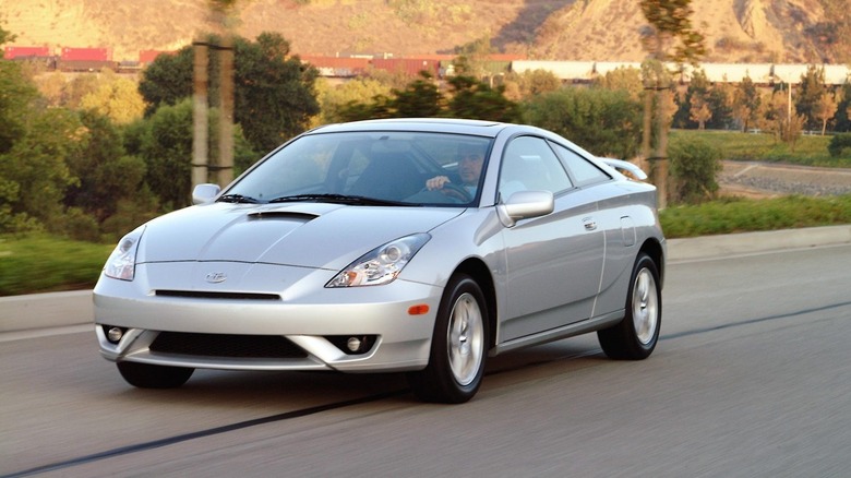 A silver 2004 Toyota Celica GT-S coupe driving on a suburban road, front three-quarter view.