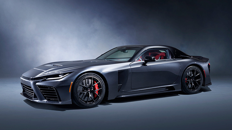 A studio front three-quarter view of a dark metallic grey Toyota GR GT concept supercar, showcasing its long front hood, aggressive fender extraction vents, and black multi-spoke wheels with red brake calipers.