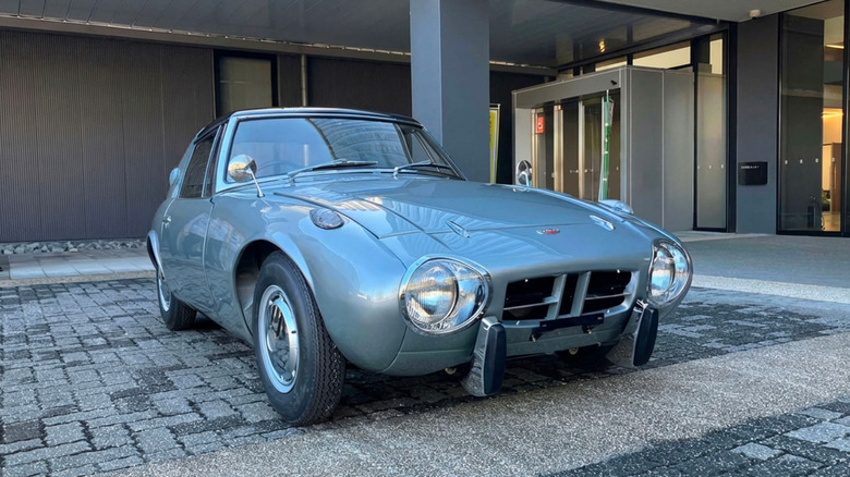 A classic silver-blue Toyota Sports 800 sports car parked on a paved driveway, front three-quarter view.