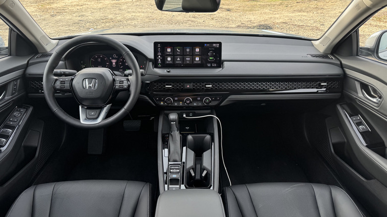A wide shot from the rear seat looking at the entire dashboard in the black interior of the Accord Hybrid Touring with some dead grass out the windshield