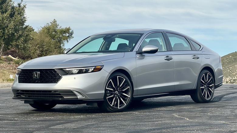 Front three quarters shot of my silver Accord Hybrid Touring parked on asphalt in front of a cloudy sky and some shrub-covered hills