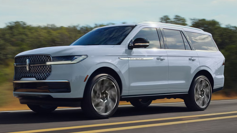 A pale blue Lincoln Navigator driving own a two-lane road