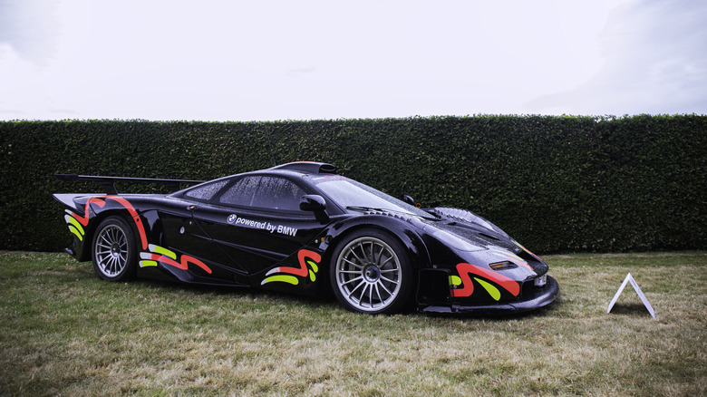 A black McLaren F1 Longtail race car on display, parked on grass with a hedge in the background.