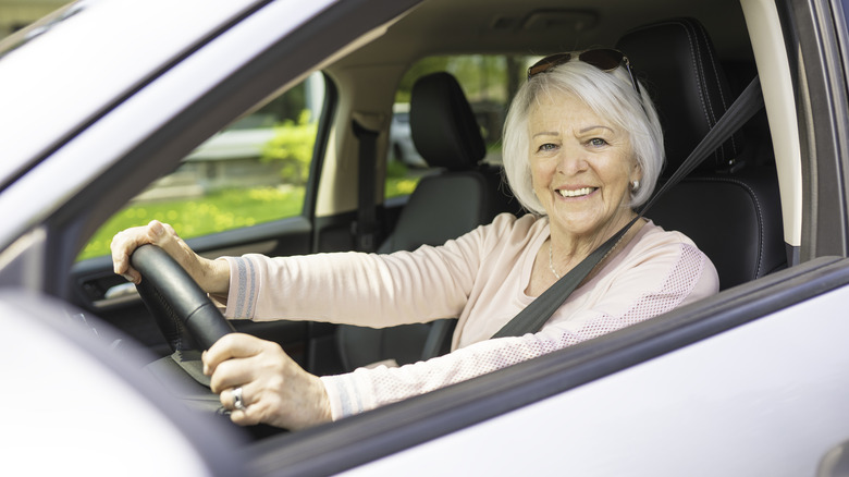 A white-haired driver smiles at the camera from behind the wheel