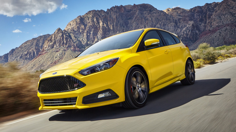 Front three quarters shot of a bright yellow Ford Focus ST driving past shrubs and desert mountains