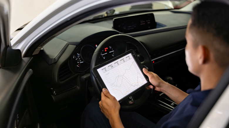 A car mechanic looking at an OBDII scan tool while sitting in the driver's seat