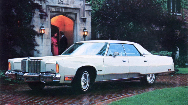 A period photo of a white 1978 Chrysler New Yorker Brougham parked in front of a luxurious estate