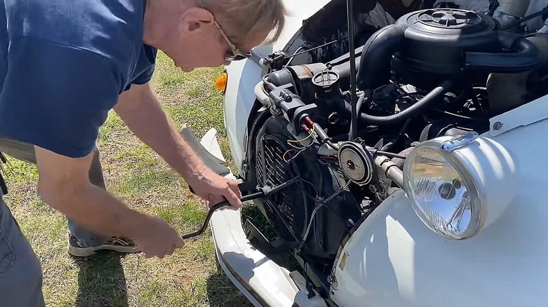 A man attempting to hand-crank a Citroën 2CV.