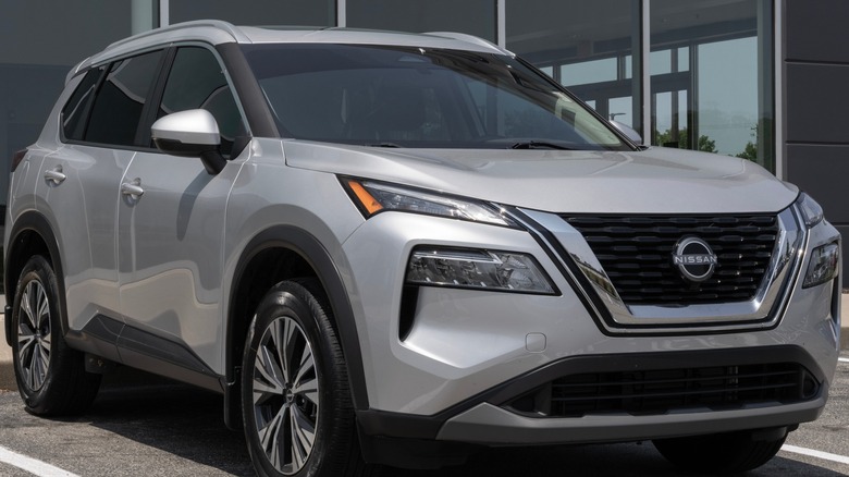 A silver Nissan Rogue in front of a showroom.