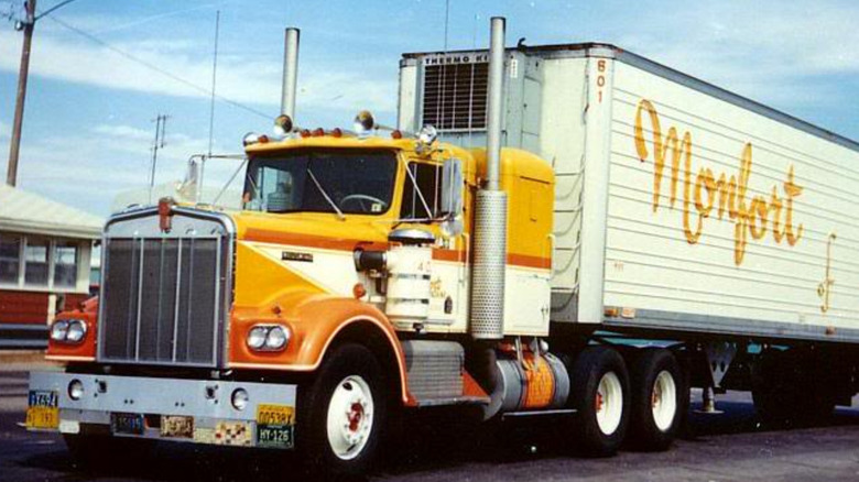 A yellow, orange, and white Kenworth Monfort truck parked outside