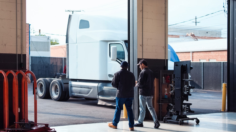 A white semi truck pulls into a maintenance bay with two people walking in the foreground