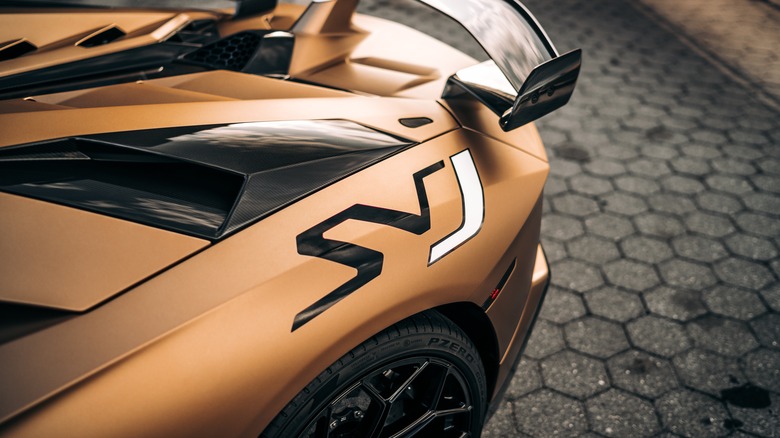 The left rear quarter of a copper-colored Lamborghini Aventador SVJ parked on hexagonal brick