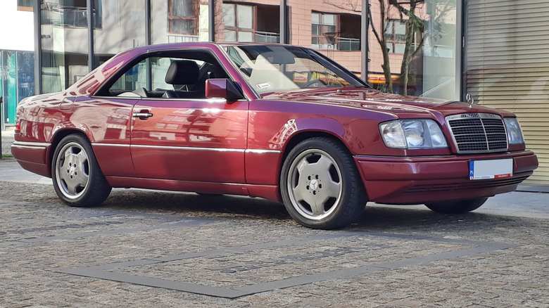 A red Mercedes-Benz 300CE coupe parked outside near buildings.