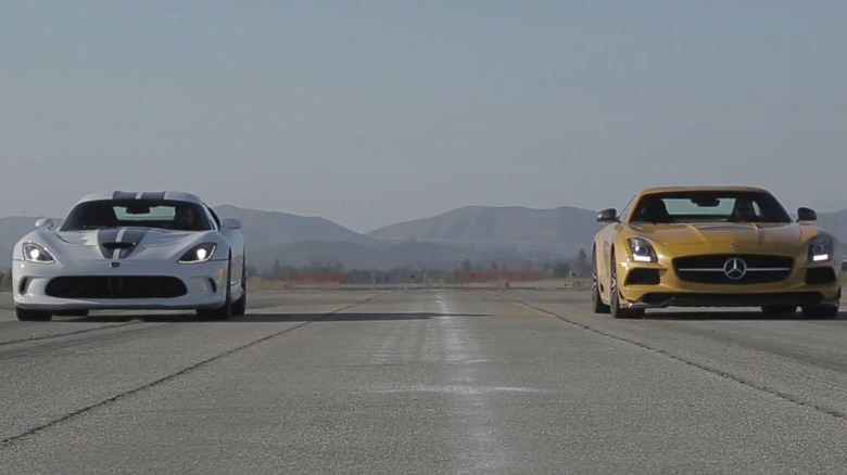 A white Dodge Viper with black racing stripes and a yellow Mercedes-AMG SLS drive toward the camera on a runway with mountains in the background
