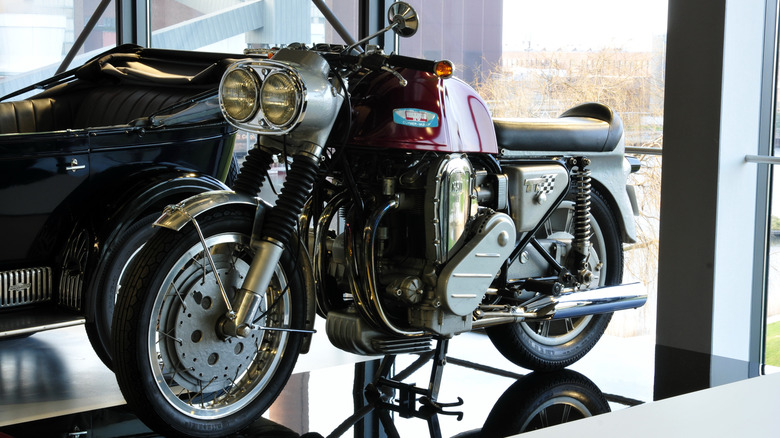 A red Clymer Münch Mammoth IV with dual headlights in a museum next to a black antique car.