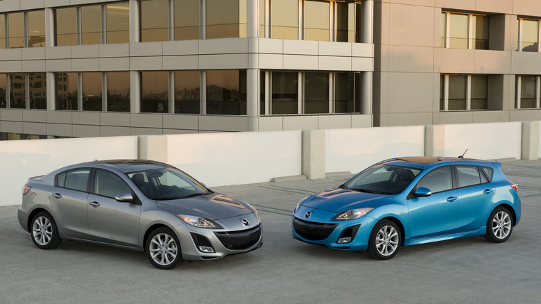 Wide shot of 2010 Mazda 3 hatch and sedan in front of an office building.