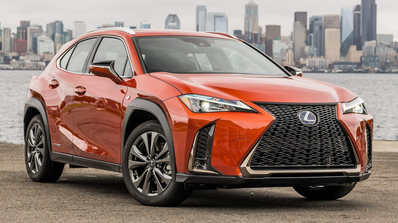 An orange Lexus UX parked by the water in front of a city skyline