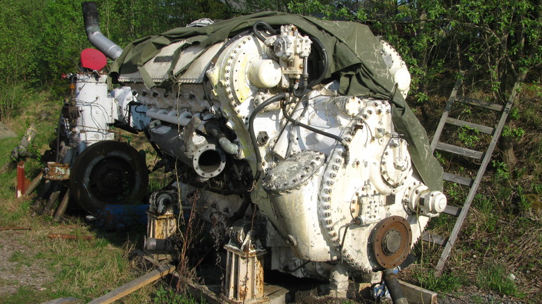 A white Napier Deltic 18 cylinder engine sits in a field, sadly rotting away