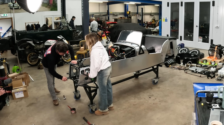 The frame of a kit car being assembled by two people