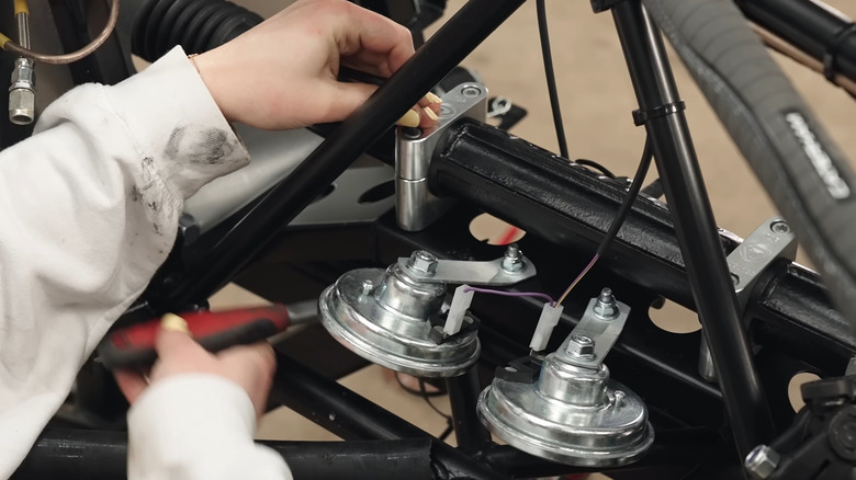 A person's hands reaching next to nuts and bolts inside a kit car