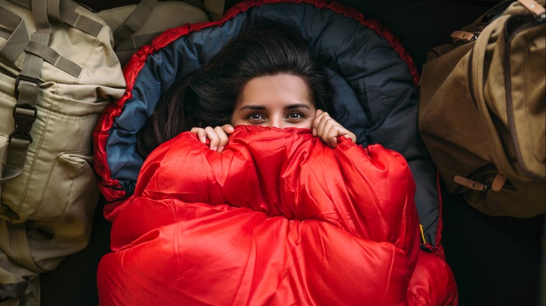 Woman in sleeping bag with it pulled up over her mouth and nose.